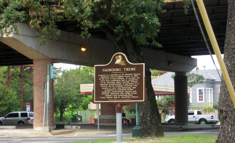 Brown plaque with light-colored text says "Faubourg Treme." It is underneath an overpass.