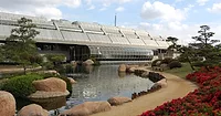 Tillman-Wastewater-Plant.jpg Water runs between a glass-walled complex and a dirt walking path lined with plants and flowers