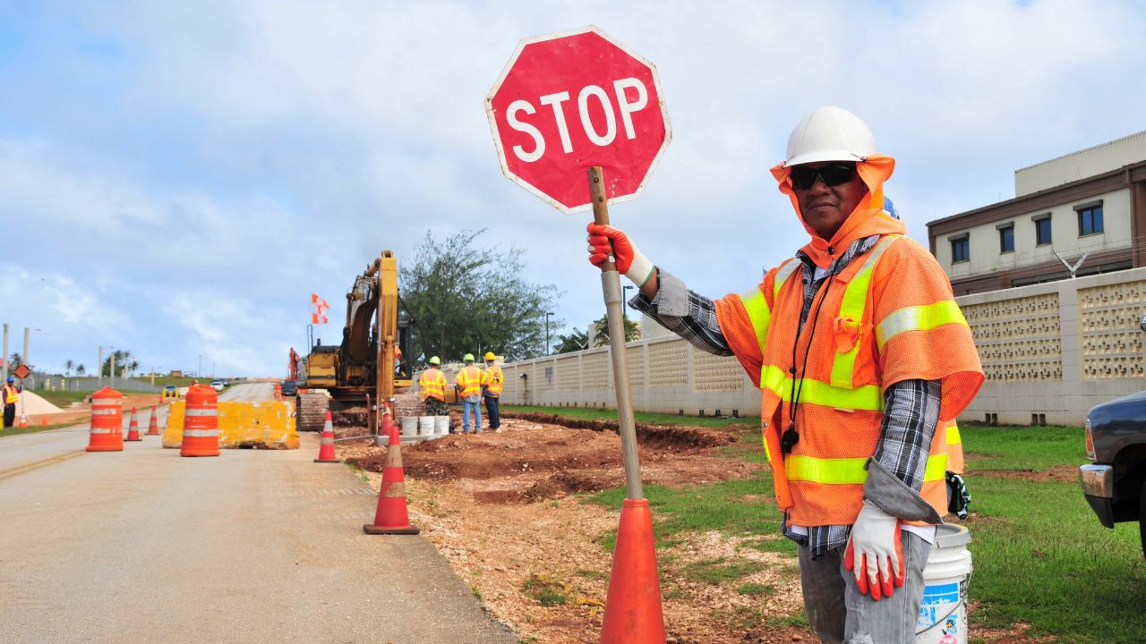 A contractor holds a stop sign for traffic control at a roadside excavation site