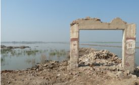 Remains of an entrance to a school stand on top of a tan hill. Behind it are a pile of rubble and floodwaters .