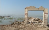 Remains of an entrance to a school stand on top of a tan hill. Behind it are a pile of rubble and floodwaters .