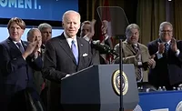 NABTU-2022-Biden.jpg President Joe Biden stands smiling in front of a podium. Five people stand behind him, clapping.