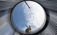 a view from within a circle of bars forming a wind turbine cage, a worker is on top, blue sky with clouds behind