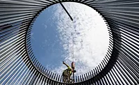 WindFarm.jpg a view from within a circle of bars forming a wind turbine cage, a worker is on top, blue sky with clouds behind