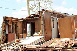 In the aftermath of Hurricane Laura, the remains of a house are shown with the roof missing and pieces of the structure, from doors to walls to furniture, piled on the ground in front of the walls that remain standing