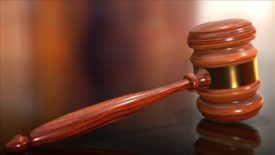 A wooden judge's gavel rests along a slightly reflective surface.