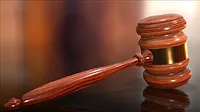 A wooden judge's gavel rests along a slightly reflective surface.