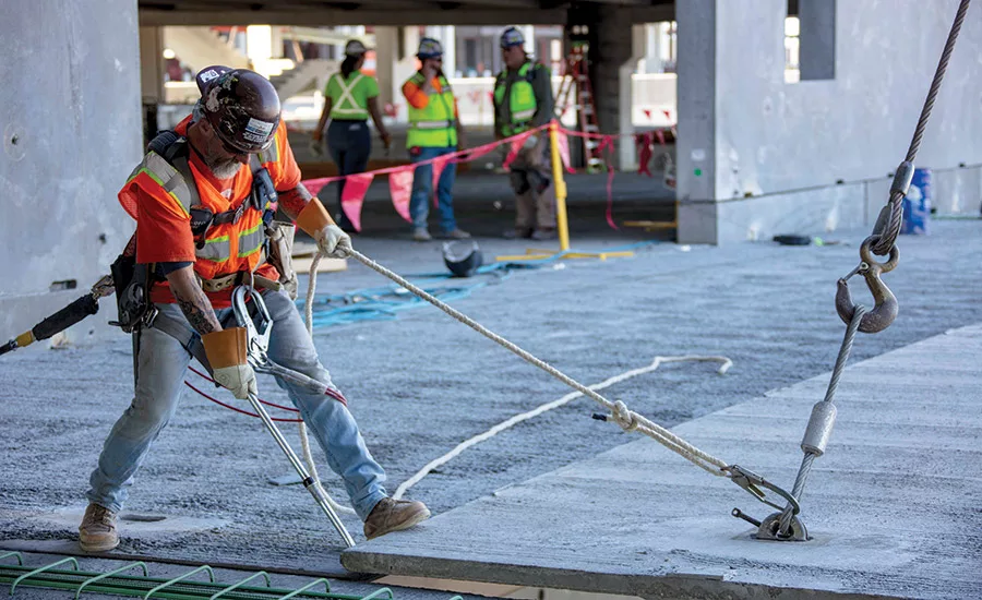 A craftworker guides a large piece of prefabricated concrete into place