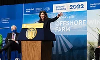 NY Hochul offshorewind NY Governor Kathy Hochul gestures with her hand as she speaks behind a dais. In the background a large banner notes a 2022 groundbreaking for South Fork Wind Farm, "New York's First Offshore Farm."