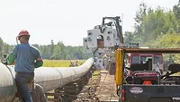 A construction worker in a red hardhat and blue shirt stands next to a white pipeline