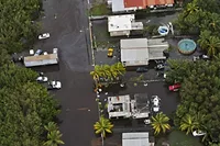 Aerial view of a neighborhood with palm trees, white roofs, cars and areas in which the road is covered by floodwater