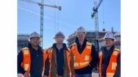 Construction workers pose for a photo on a project site with tower cranes behind them