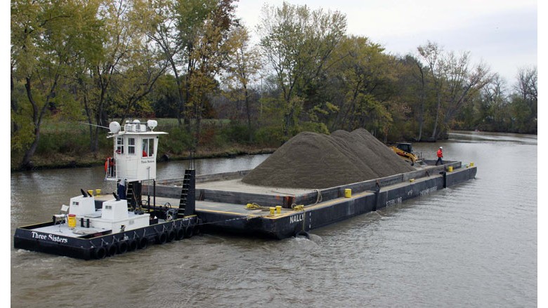 A barge carrying coal floats on a waterway with trees in the background