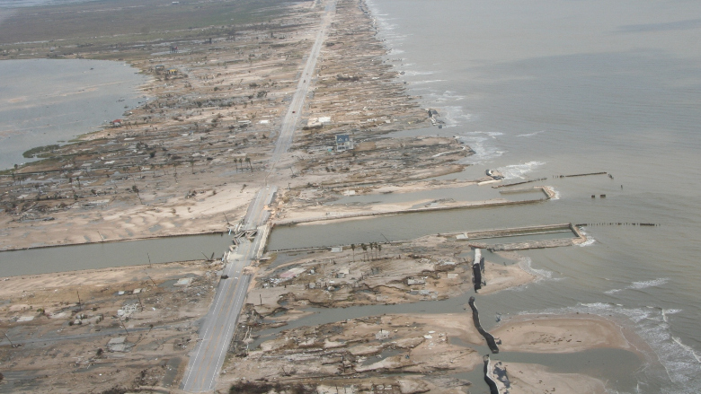 An overhead view of the Bolivar Peninsula after Hurricane Ike, showing a strip of muddy land surrounded on either side and cut in the middle horizontally by water. A road runs from top to bottom at a slight diagonal.