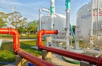 Stuart Florida PFAS KimleyHorn In this outdoor scene, orange red pipes shown in the foreground connect to two white water storage tanks. Trees and grass are seen in the background amidst a blue sky.