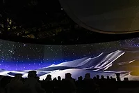 Silhouttes of attendees sit in chairs watching the image of an iceberg across a wide screen