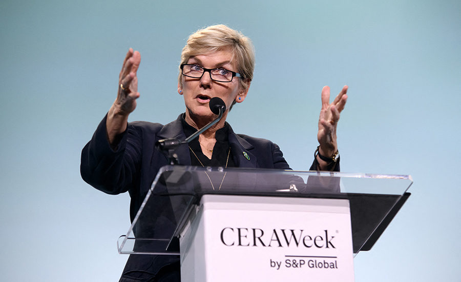 Energy Secretary Jennifer Granholm wearing a black top stands in front of a podium with a clear top. The text on the podium says "CERAWeek by S&P Global"