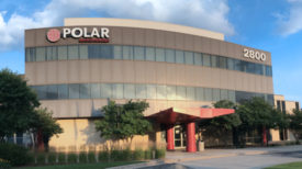 A building with a red entrance and two strips of windows running horizontally across with the Polar logo on the building's upper left hand corner. 