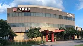 A building with a red entrance and two strips of windows running horizontally across with the Polar logo on the building's upper left hand corner. 
