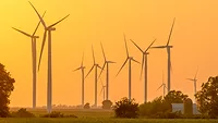 Wind turbines A group of 11 wind turbines are displayed across an expanse of green land, with an orange sunset in the background.
