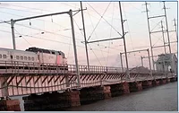 A New Jersey Transit train crosses over a bridge, with a pink and blue sky in the background.