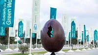 COP29 A sculpture of an egg with a crack is shown in a courtyard with green banners displaying COP29 logos