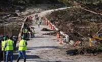 Texas Flood Workers wearing hardhats and yellow vests clean up in the aftermath of a flood, with debris seen on either side of a bridge