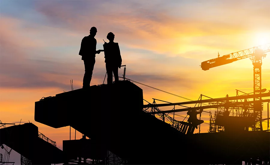 Silhouette of two construction professionals on a jobsite at sunset with cranes in the background, illustrating ABC’s August 2025 report showing backlog at 8.5 months and contractor optimism holding steady.