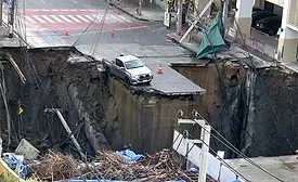 Pickup truck at edge of large Bangkok sinkhole exposing metro tunnels under construction.