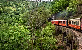Train entering a tunnel on a stone viaduct in India’s Himalayan foothills, illustrating the engineering challenges of building new cross-border rail lines into Bhutan.