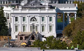 Construction workers on top of the U.S. Treasury watch as work continues on a largely demolished portion of the White House's East Wing.