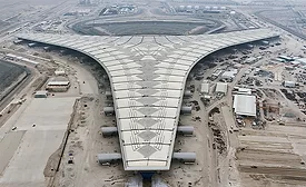 Aerial view of Kuwait International Airport’s Y-shaped Terminal 2 building under construction with surrounding airfield and access roads visible.  