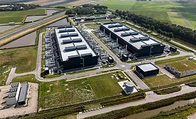 Aerial view of a large data-center complex surrounded by access roads and green fields.
