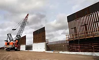 Steel border barrier panels installed with crane along U.S.–Mexico border.