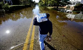 Flood image from Crisfield, Maryland, with someone carrying bottled water and coffee as they walk down a road covered in water