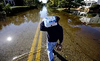 Crisfield Flooding ENR Flood image from Crisfield, Maryland, with someone carrying bottled water and coffee as they walk down a road covered in water