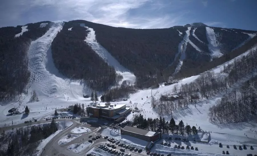 A photo of Killington Mountain resort shows a mountain with snowy trails running down and a parking lot and building in the foreground