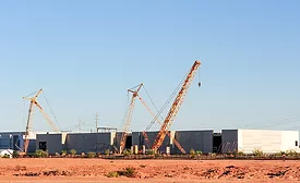 Cranes work on a large industrial construction site with multiple buildings under construction.