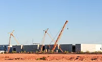 ABC Construction Needs Report Cranes work on a large industrial construction site with multiple buildings under construction.