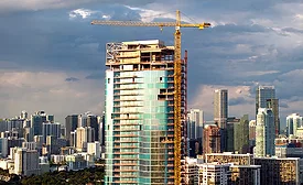 High-rise tower under construction with crane in dense urban skyline.