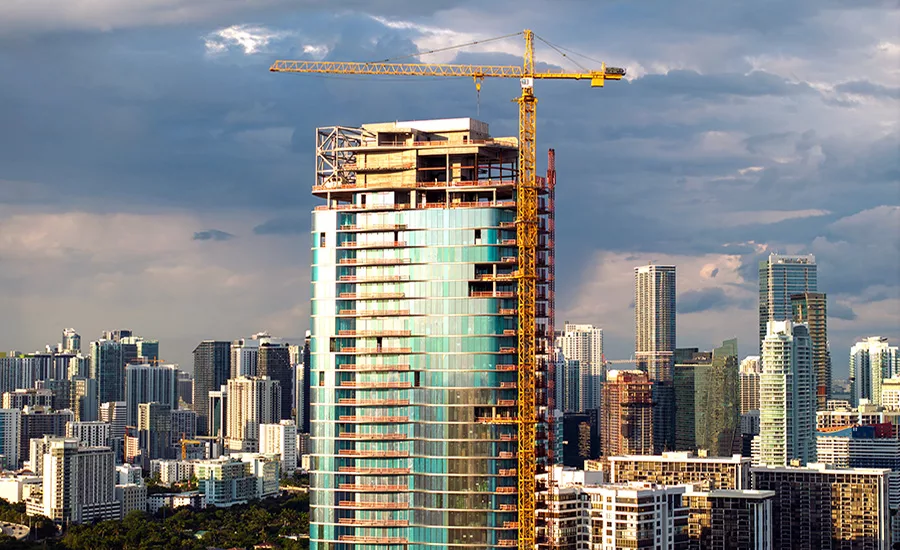 High-rise tower under construction with crane in dense urban skyline.