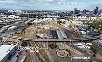 Aerial view of Burnham Yard in Denver with 8th Avenue Viaduct, former rail yard structures and downtown skyline in the distance.