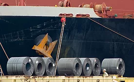 Steel coils unloaded at a port in front of a cargo vessel, illustrating tariff exposure on imported construction materials.