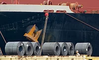 Steel coils unloaded at a port in front of a cargo vessel, illustrating tariff exposure on imported construction materials.