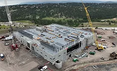 Aerial view of a semiconductor manufacturing facility under construction with cranes and structural steel framing visible.
