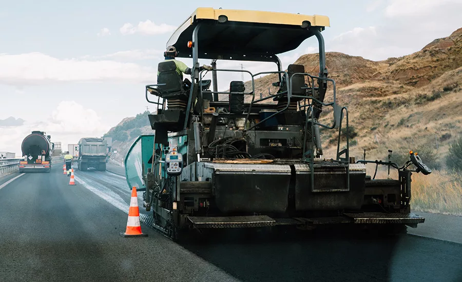 Photos shows an asphalt paver and other construction equipmets at work on a road project.