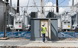 Worker inspects large power transformers at electrical substation.