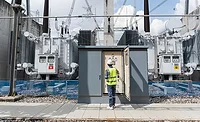 Worker inspects large power transformers at electrical substation.