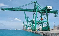 Ship-to-shore cranes along a port berth at Guam with containers and ocean in view.