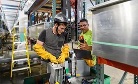 Workers perform electrical installation and testing inside an industrial facility.